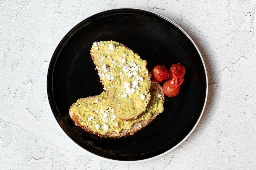Avocado toast with feta and blistered tomatoes on a black plate