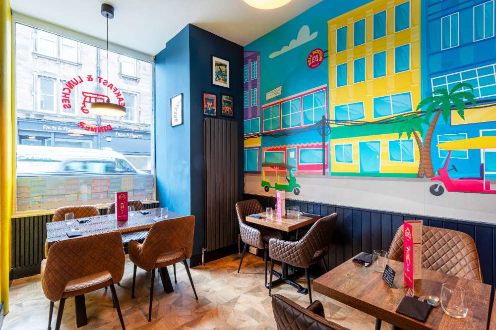 The window corner at Bell Bottom Eatery — Delhi street mural with tuk-tuk and pink scooter, tenement view through the glass