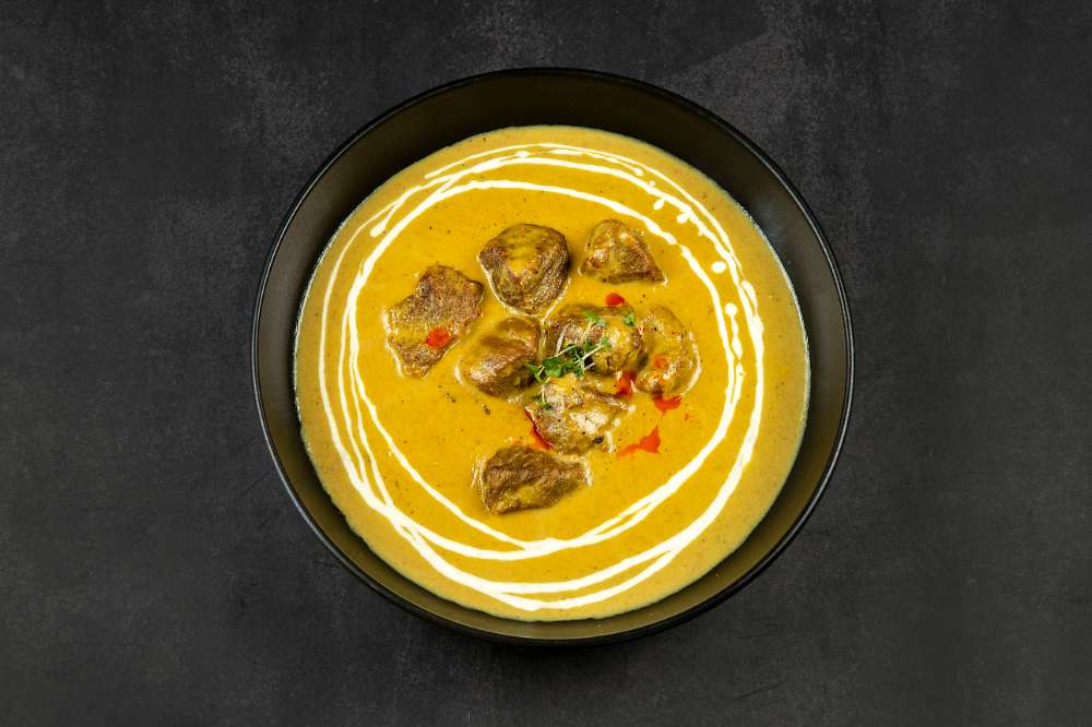 A slow-cooked yellow curry swirled with cream in a black bowl