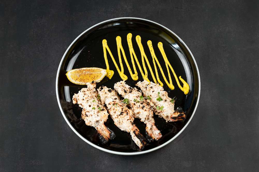 Chargrilled malai chicken skewers with a saffron drizzle on a black plate